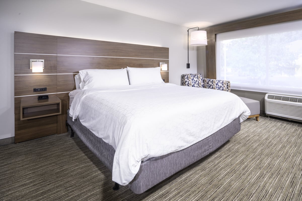 A modern hotel room with a large bed, a nightstand, a lamp, and a window with a view.