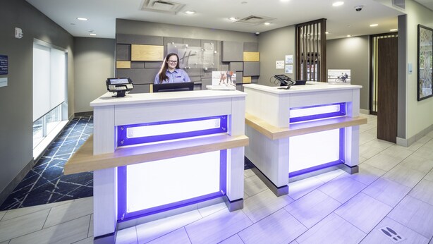 Un área de recepción con dos mostradores, cada uno con una computadora y un teléfono. A la izquierda, hay un ventanal grande, y el piso tiene un diseño con motivos.