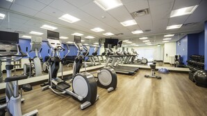 Un gimnasio con diferentes máquinas de ejercicio, espejos y suelo de madera.