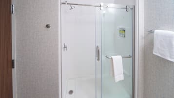 Cabina de ducha con paredes de vidrio y una toalla blanca colgada del picaporte.