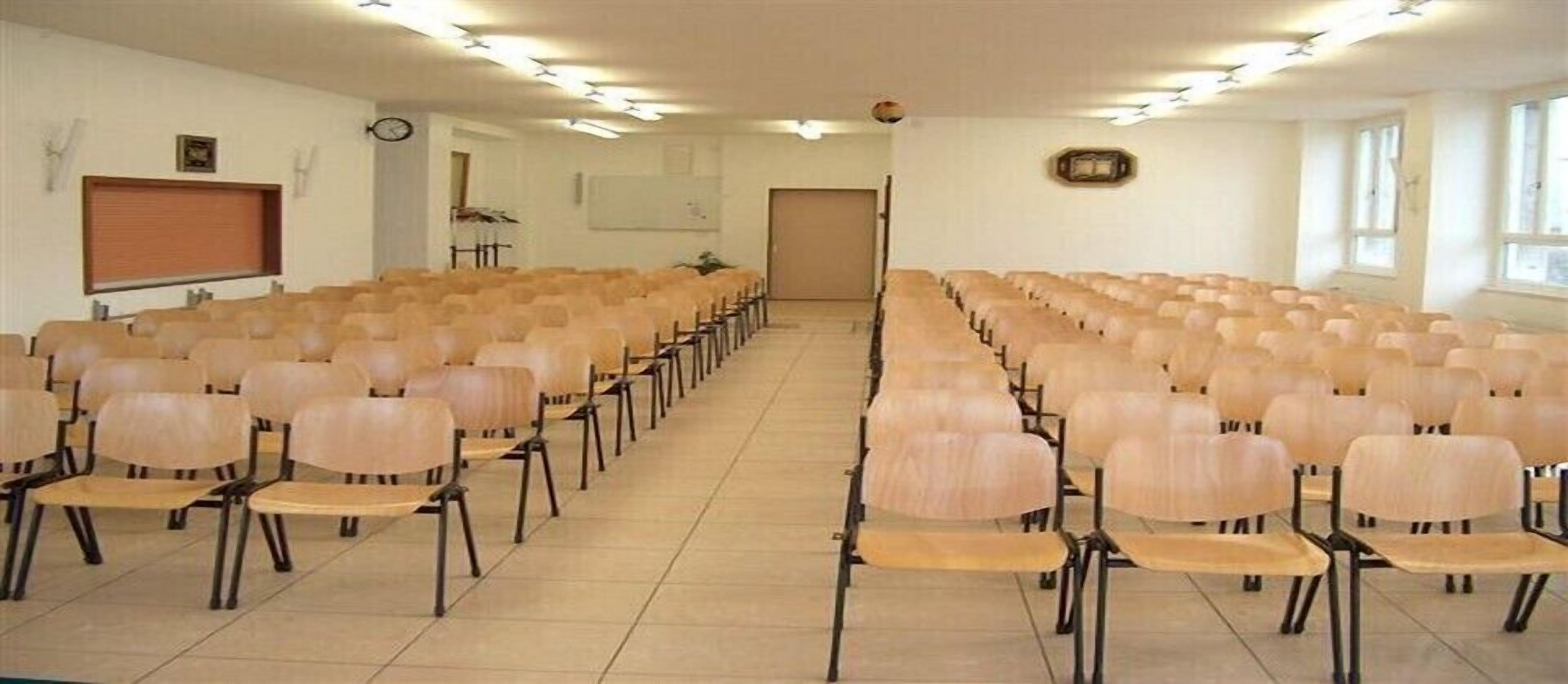 A conference room with rows of chairs, a projector screen, and a clock on the wall.