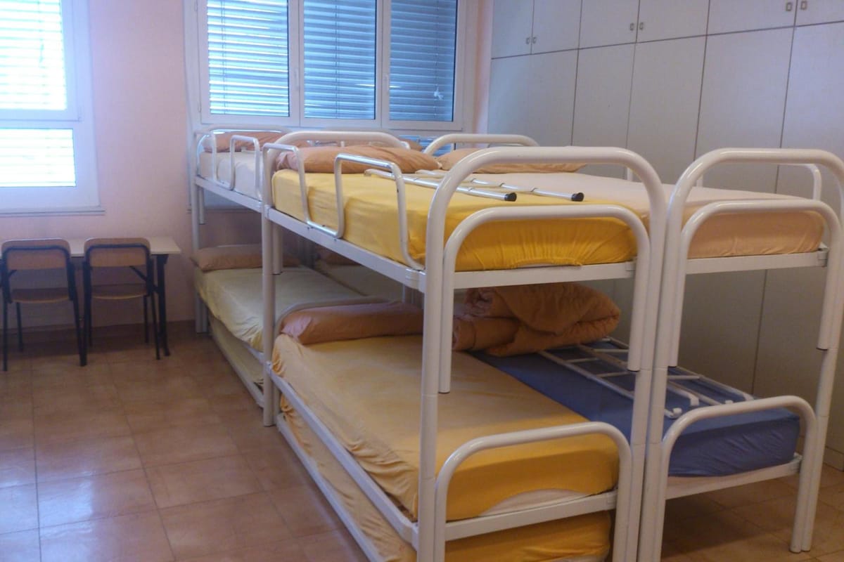 A bunk bed room with a window, chairs, and a tiled floor.