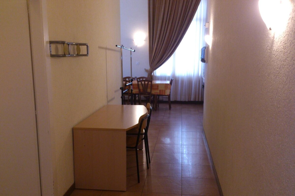 A narrow hallway with a dining area at the end featuring a table and chairs.