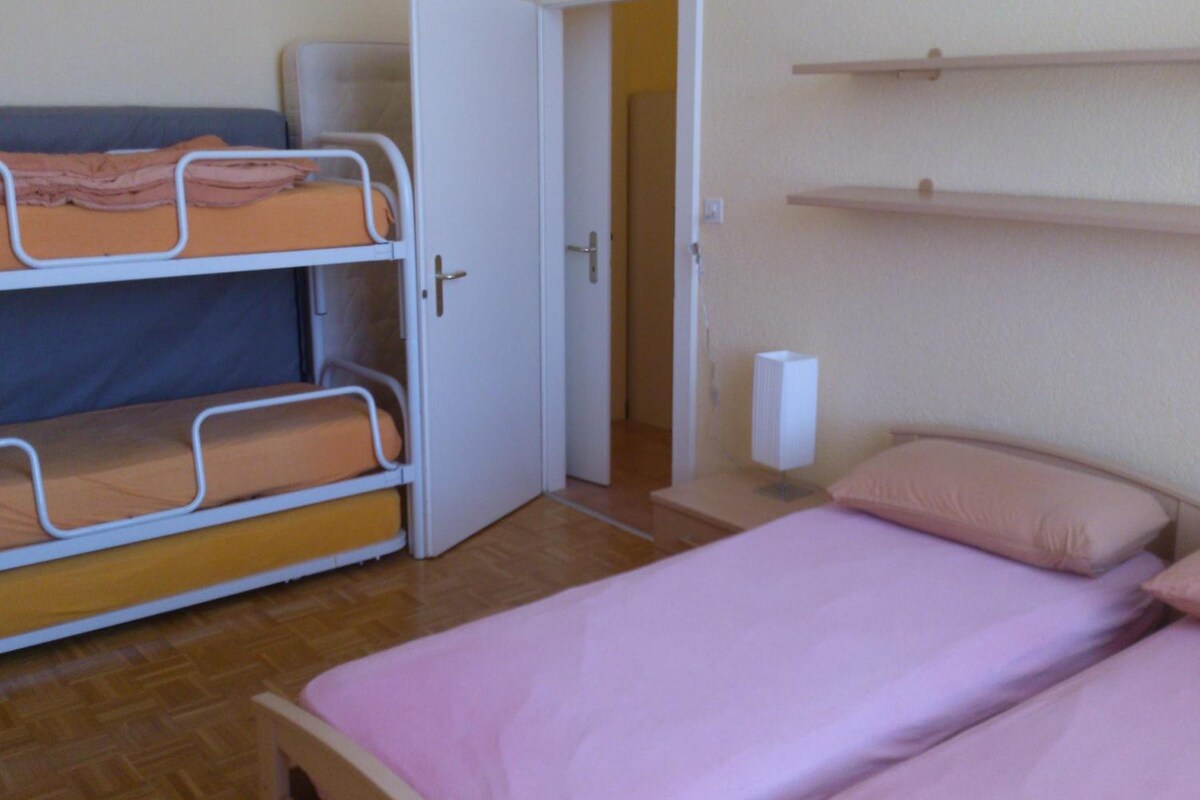 A room with bunk beds, a single bed, a door, a shelf, and a wall socket.