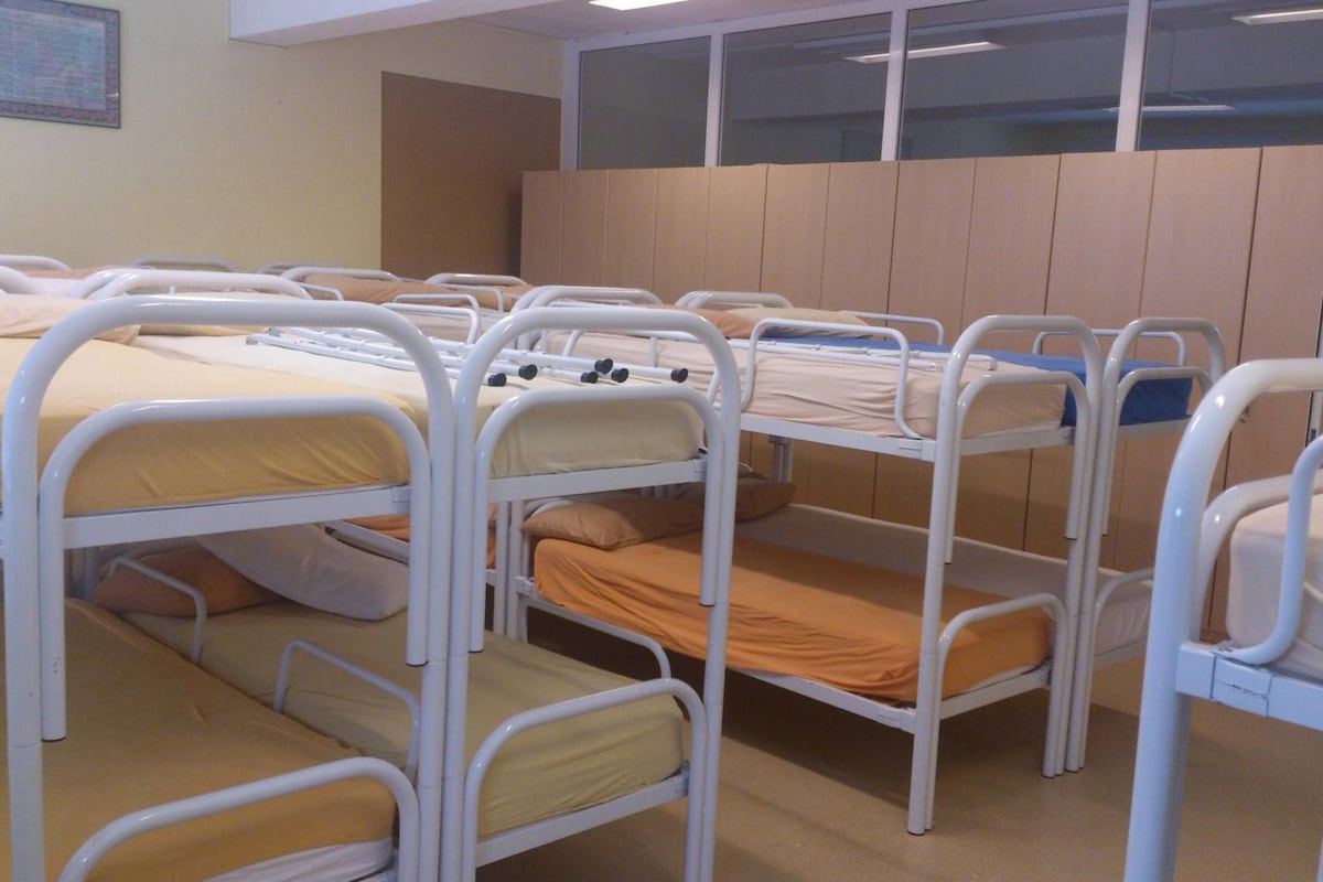 A room with bunk beds arranged in a row, each with a mattress and pillows.