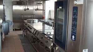 Een professionele keuken met roestvrijstalen apparatuur, waaronder een grote oven en een koelkast met bedieningspanelen.