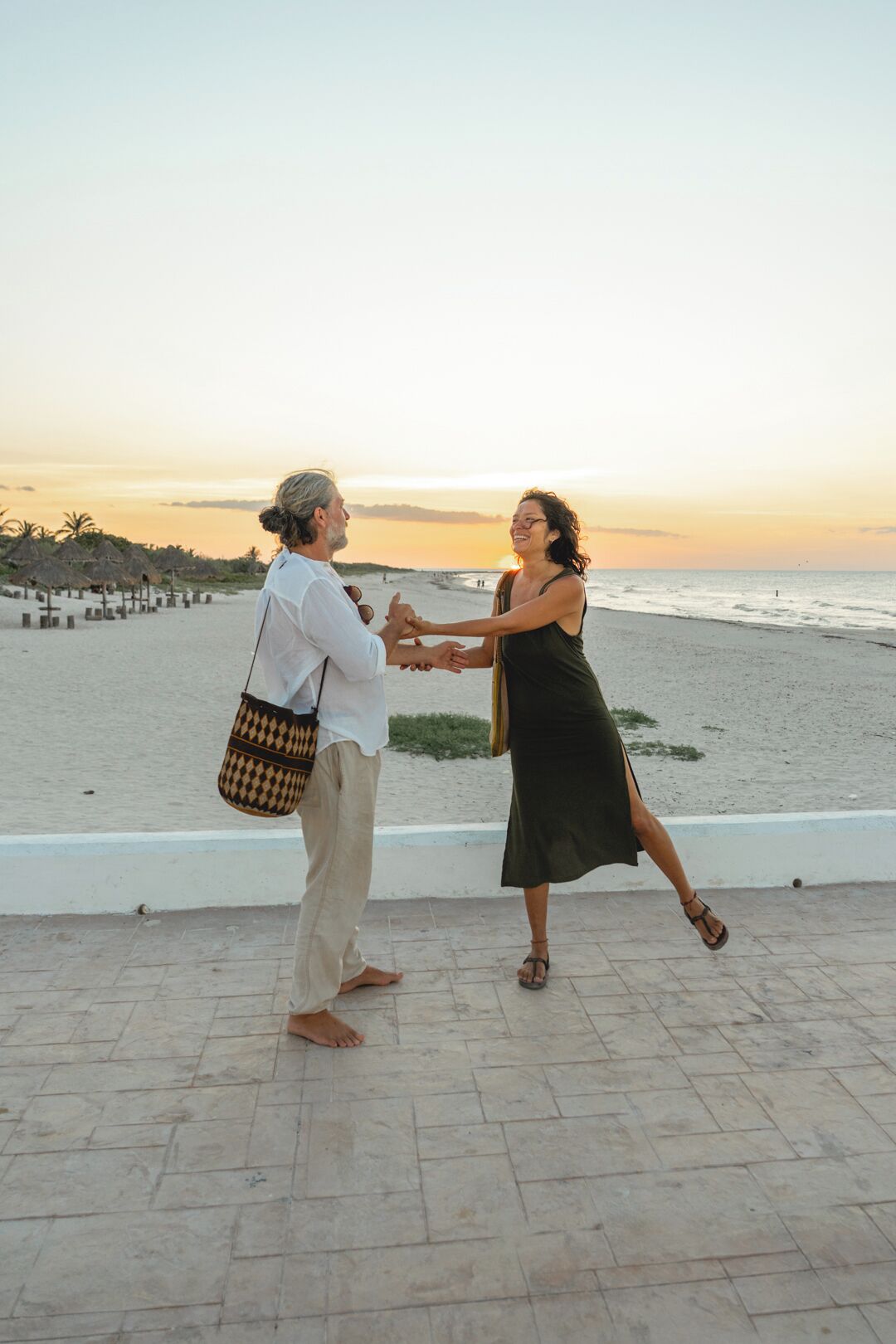 Dos personas bailando en una zona pavimentada, con una playa y el océano al fondo.