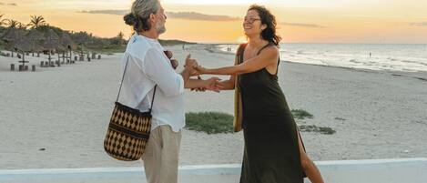 Two people dancing on a paved area with a beach and ocean in the background.