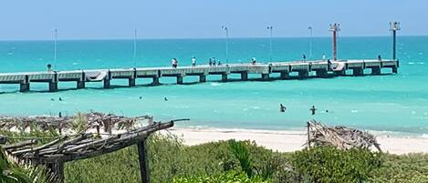 A pier extending into turquoise waters with people walking along it.