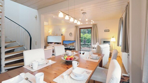 A modern hotel room with a wooden dining table set for breakfast, a TV, and a balcony with curtains. - Holiday house near Anne (sauna, forest, lake) (Kirchheim)