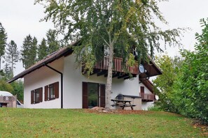 Un chalet de dos pisos con balcón, antena parabólica y mesa de picnic en el jardín.