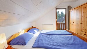 A small, cozy room with a sloped ceiling and wooden walls. There are two beds with blue bedding and a wooden wardrobe. - Holiday house near Anne (sauna, forest, lake) (Kirchheim)