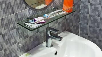 Et badeværelse med en hvid vask, en glashylde med toiletartikler og et spejl.