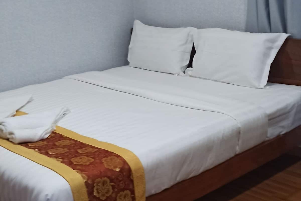 A neatly made bed with white linens and a red floral bedspread, a wooden headboard, a power outlet on the wall, and a blue curtain.