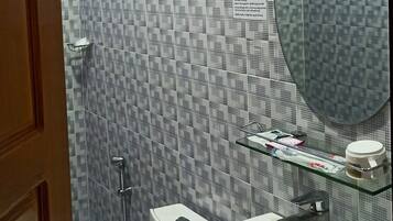 Uma casa de banho com lavatório branco, espelho, chuveiro e sanita.