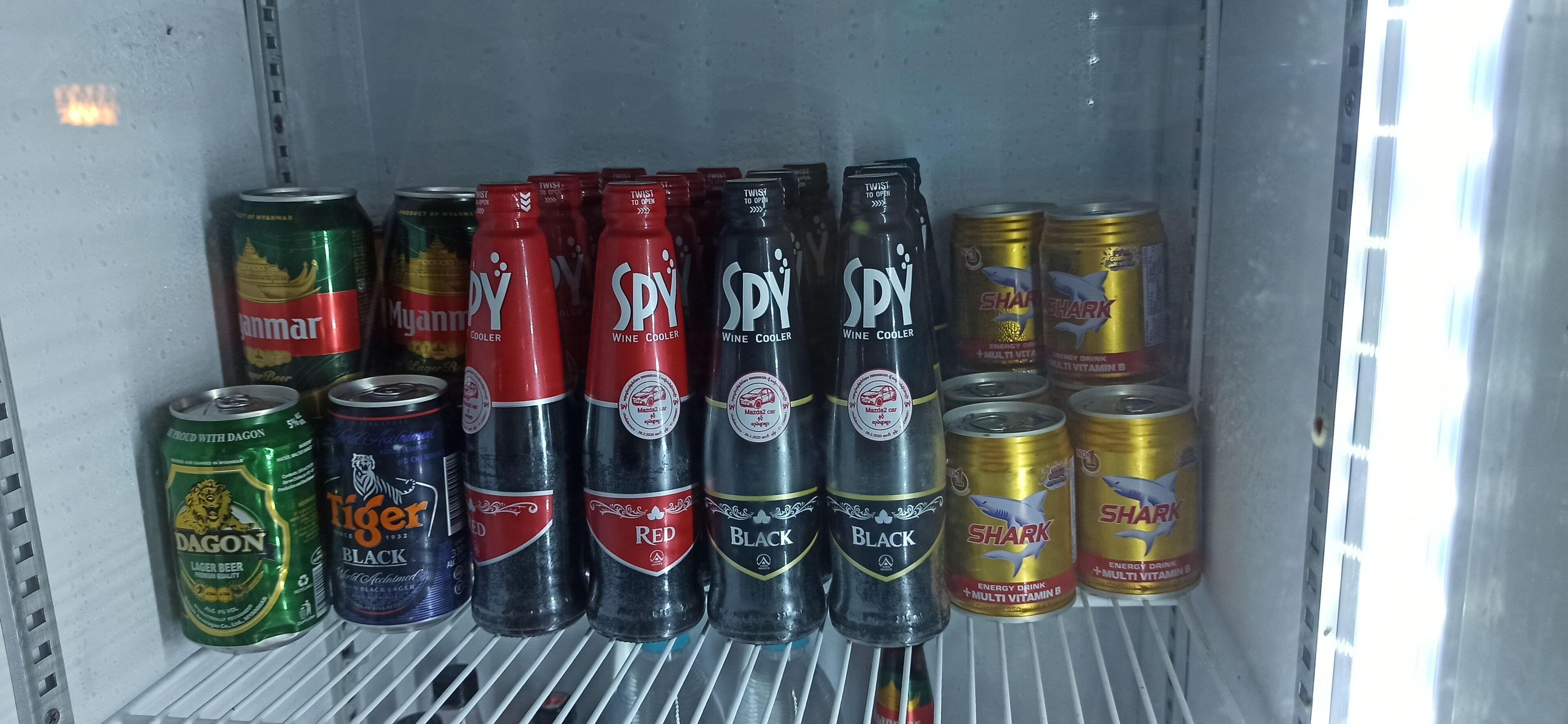 Et køleskab fyldt med diverse drikkevarer, herunder øl, wine coolers og energidrikke.