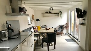 A modern kitchen with white cabinets, a dining area with a wooden table and chairs, and a large window providing natural light. - Vacation home with 3 bedrooms, furnished. Garden, 2 bathrooms, 2 kitchens, 200 meters from the beach (Egmond aan Zee)