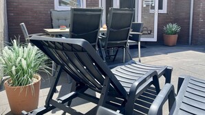 A patio area with outdoor furniture, including chairs and a table, a potted plant, and a brick wall with windows. - Vacation home with 3 bedrooms, furnished. Garden, 2 bathrooms, 2 kitchens, 200 meters from the beach (Egmond aan Zee)