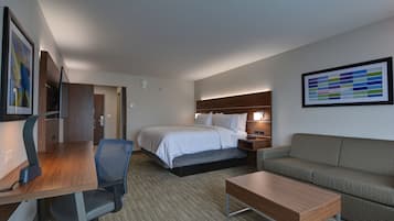 A hotel room with a bed, a desk, a chair, a sofa, and a nightstand with a lamp.