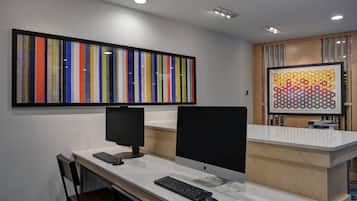 A modern office space with two desks, each with a computer monitor, keyboard, and mouse. There is a framed artwork above the desks and a wooden reception desk with a patterned glass panel.