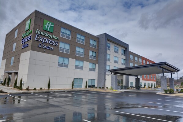 A Holiday Inn Express & Suites hotel with a modern design, featuring a large parking lot and a covered entrance.