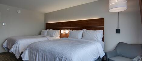 Een hotelkamer met twee bedden, een bank, een lamp en een bedieningspaneel aan de muur.