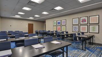 A conference room with multiple tables and chairs, a patterned carpet, and framed artwork on the walls.