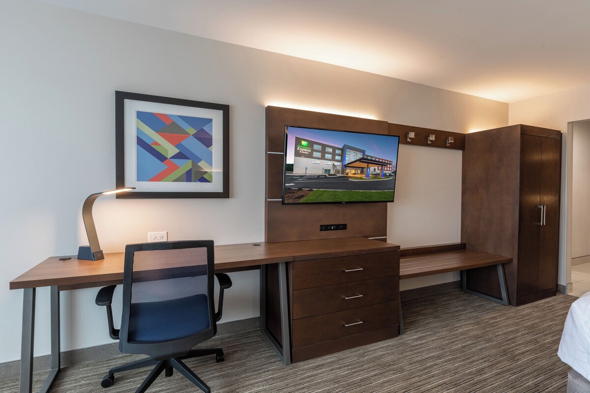 A hotel room with a desk, chair, television, and a framed picture on the wall.