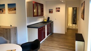 A modern kitchen with red cabinets, a black countertop, and a built-in stove. There is a dining area with a white table and black chairs. The room has wooden flooring and white walls.