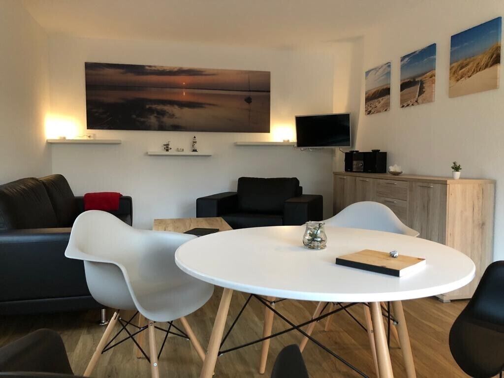 Ett modernt vardagsrum med ett runt, vitt bord, två vita stolar, en svart soffa och en tv som är monterad på väggen.