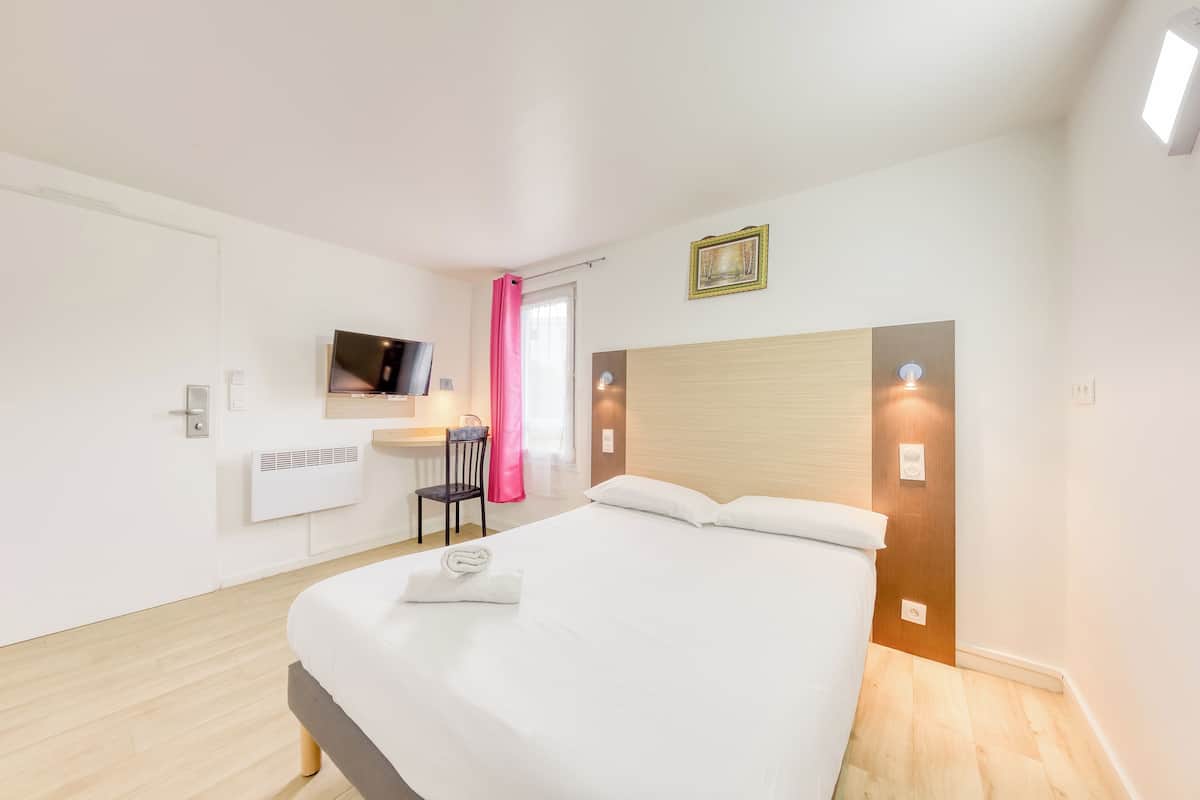Een moderne hotelkamer met een groot bed, een bureau met stoel, een flatscreen televisie aan de muur en een raam met roze gordijnen.