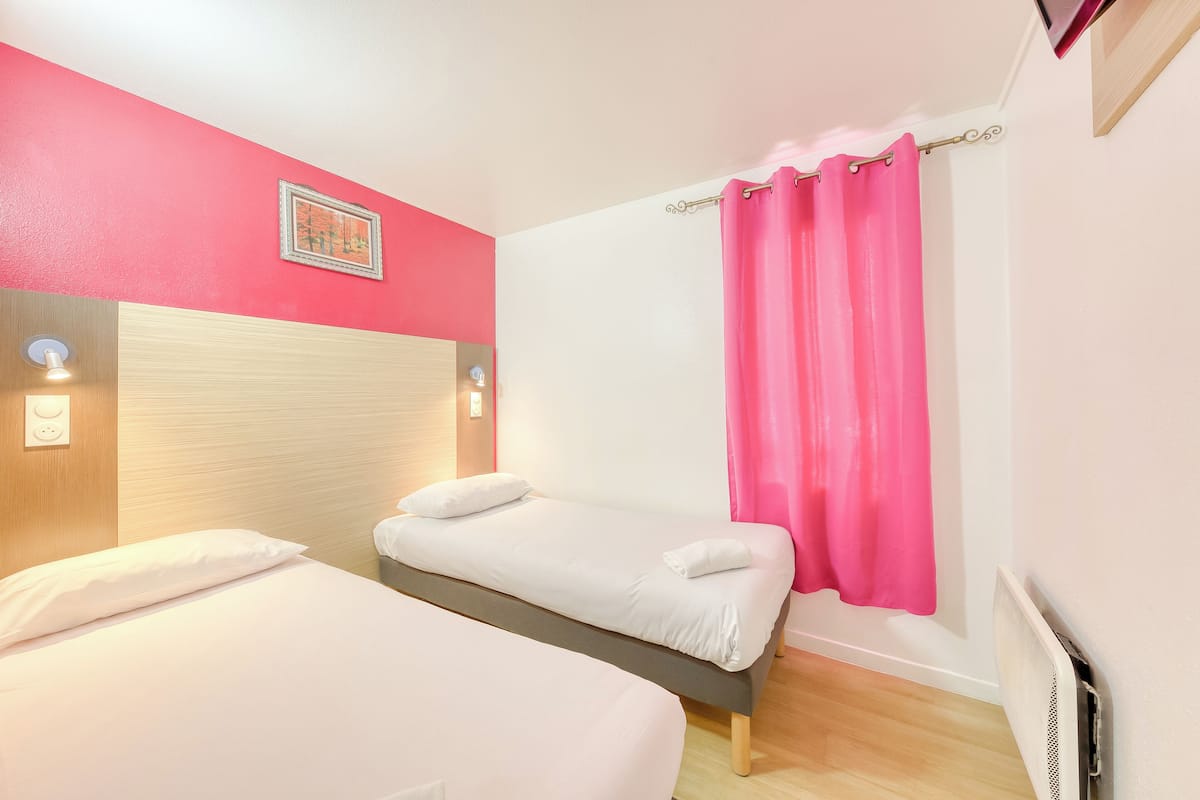 Een hotelkamer met twee bedden, een roze gordijn en een lijst met een afbeelding aan de muur.