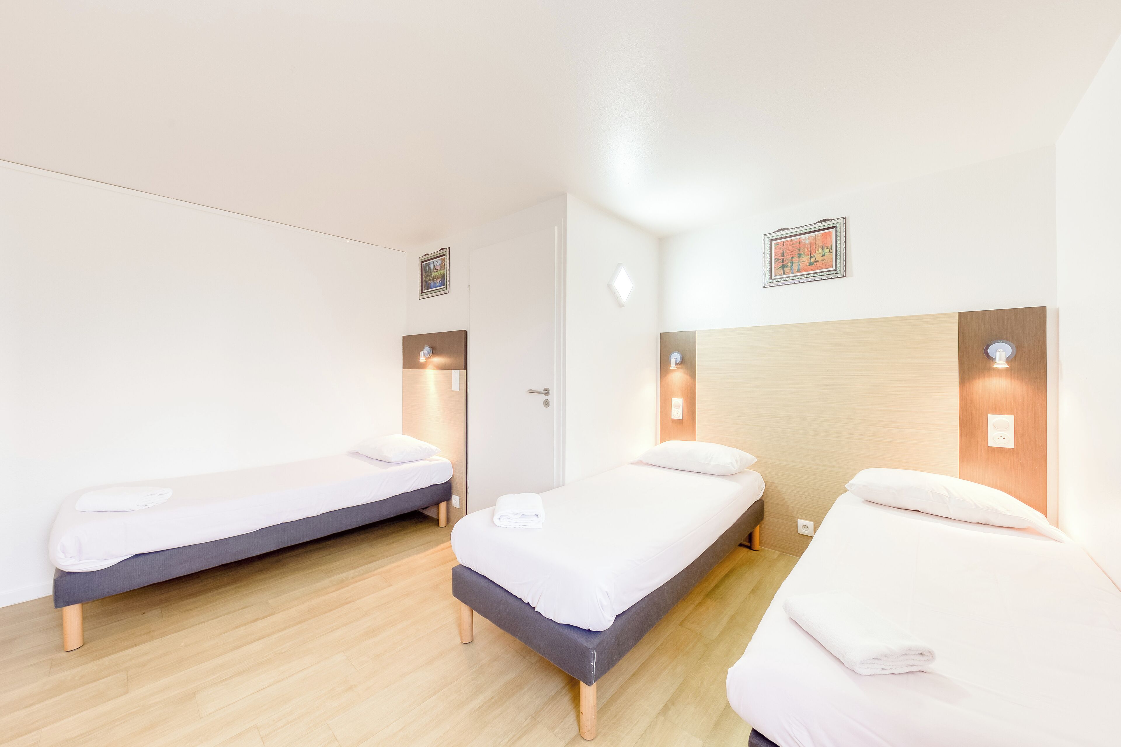 A hotel room with two single beds, a wooden floor, and a door.