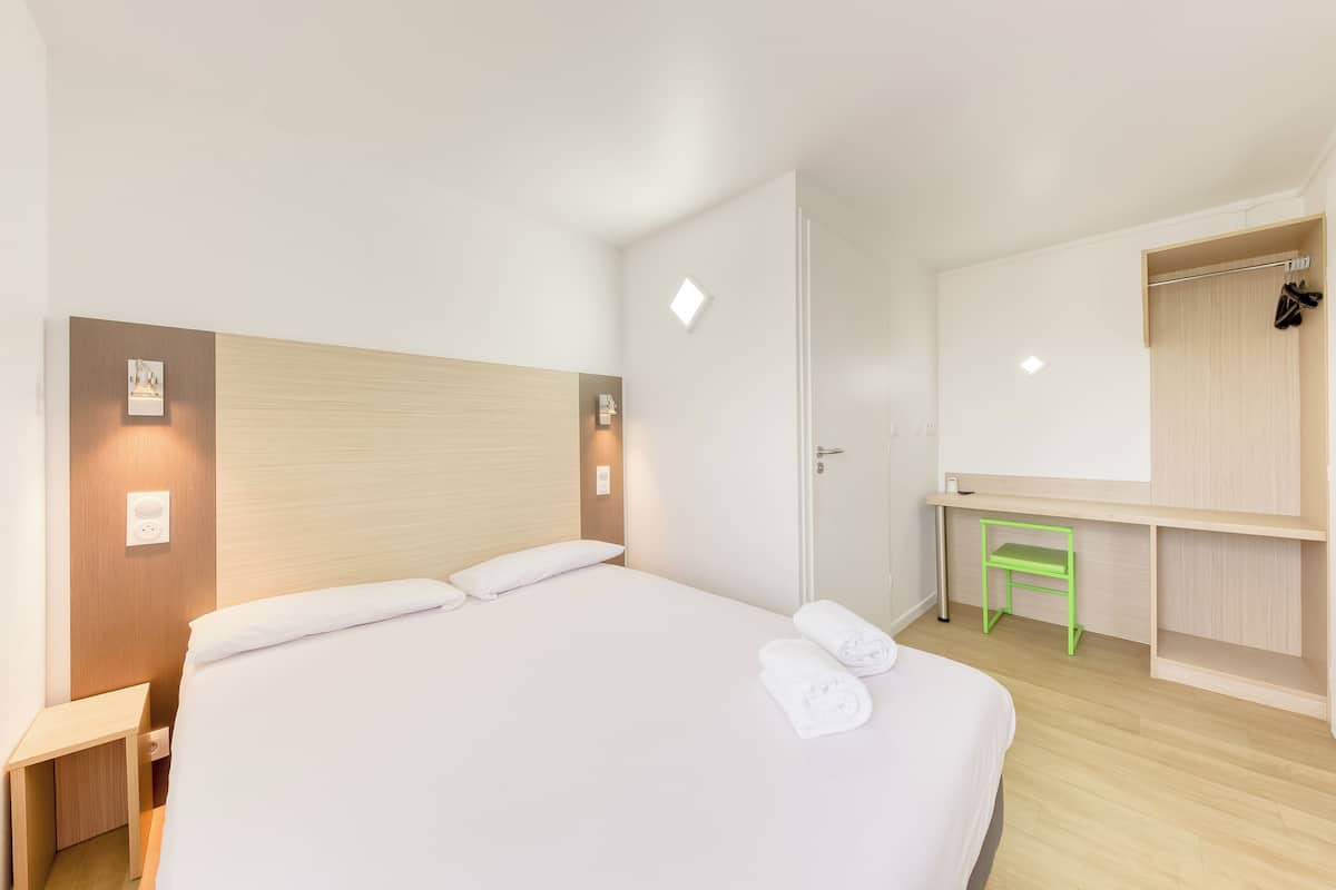 Een hotelkamer met een bed, nachtkastje, groene stoel, kledingkast en spiegel.