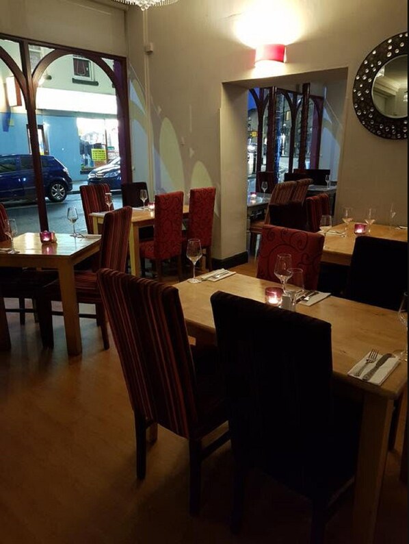 A restaurant with tables and chairs, a view of the street outside, and a mirror on the wall. - Ambassador hotel (Neath)