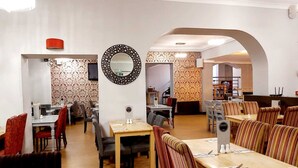 Um restaurante com várias áreas de refeição, incluindo cabines e mesas. Há espelhos decorativos nas paredes e um papel de parede estampado.