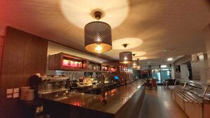 Uma área de bar com balcão, prateleiras com garrafas e luminárias pendentes.