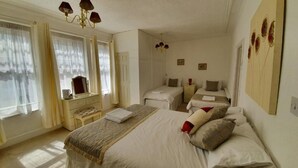 Quarto de hotel com uma cama grande, duas camas menores, uma escrivaninha e uma cadeira.