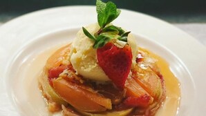 Um prato de sobremesa com uma bola de sorvete, uma morango e uma folha de hortelã por cima.