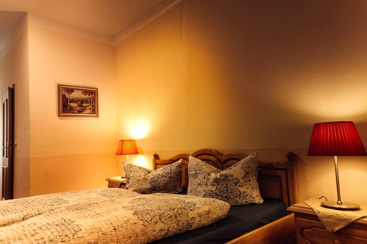 A neatly made bed with patterned bedding, a bedside table with a lamp, and a framed picture on the wall.