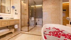 A modern bathroom with a marble floor, a glass-enclosed shower, a bathtub with rose petals, and a large mirror. - Oriental Ventura Hotel (Lishui)