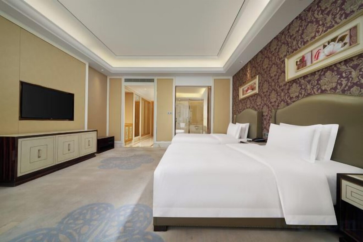 Ein Hotelzimmer mit einem großen Bett, einem Flachbildfernseher, einer Minibar und einem durch eine geöffnete Tür einsehbaren Badezimmer.