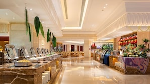 A buffet area with multiple food stations, a seating area with tables, and a decorative plant display. - Oriental Ventura Hotel (Lishui)