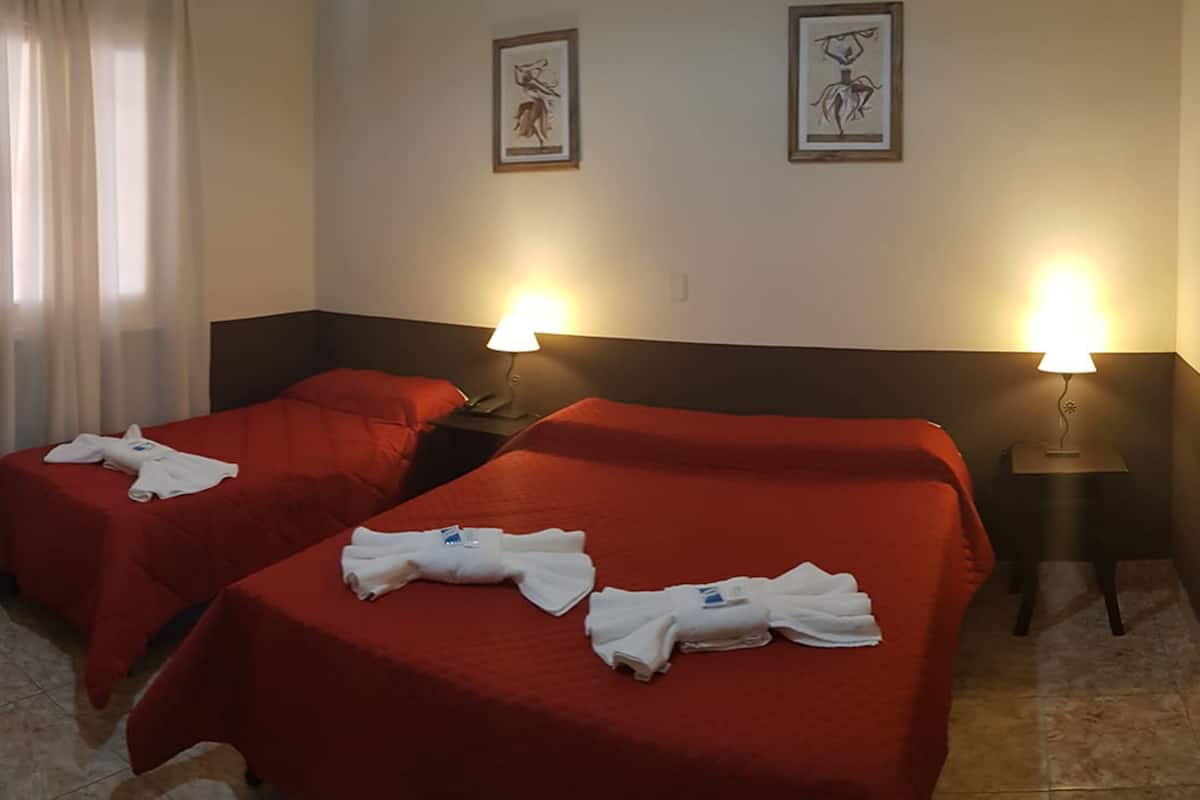 Habitación de hotel con dos camas, cada una con colcha roja y toallas blancas. Hay dos lámparas de pared a cada lado de las camas.