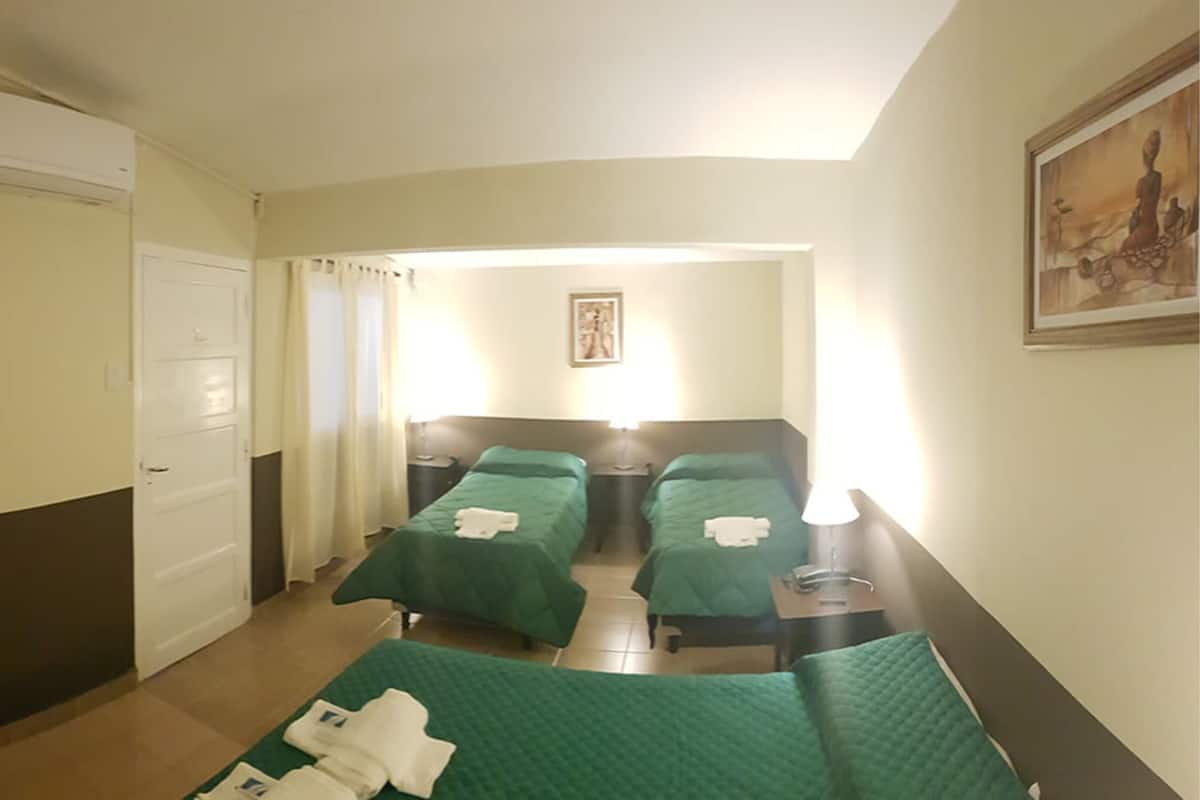 Habitación de hotel con dos camas individuales, una puerta, un equipo de aire acondicionado, un cuadro en la pared y una ventana con cortinas.