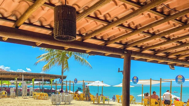 Un restaurante frente a la playa con terraza, piso de baldosas y vista al mar.