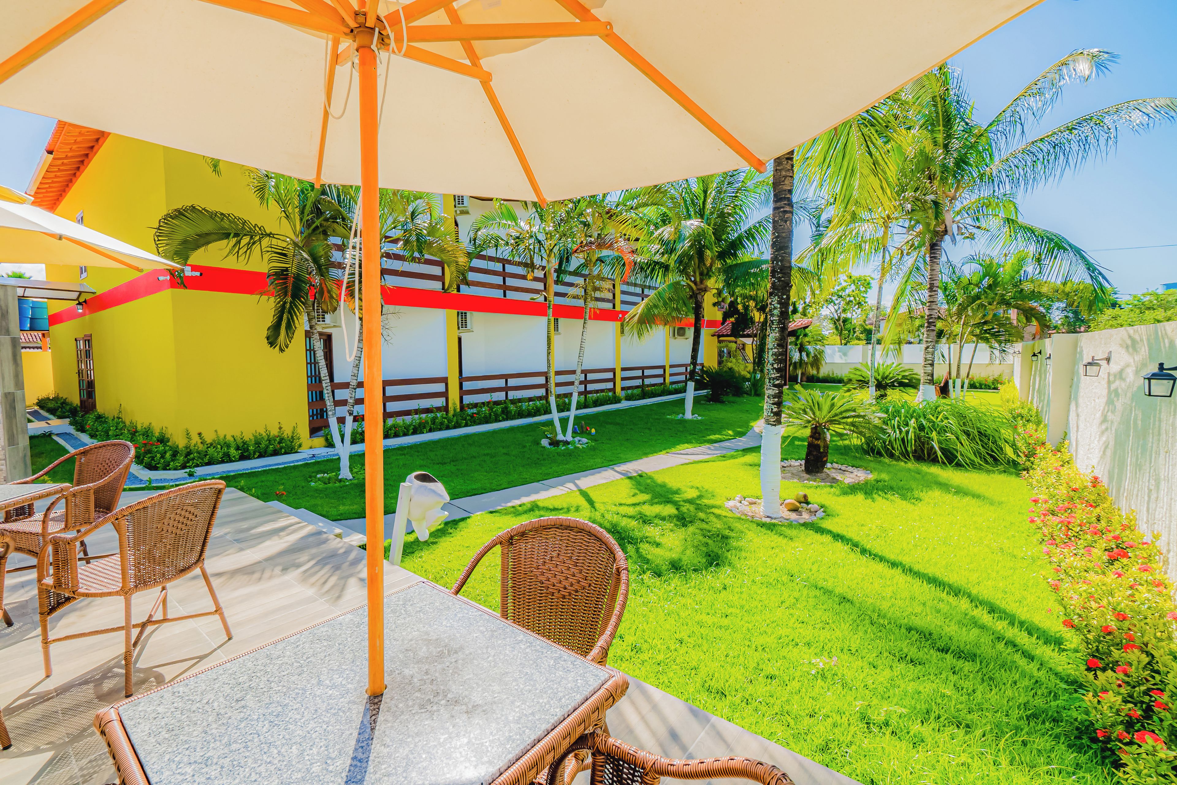 Un patio al aire libre con una mesa y sillas, rodeado de un césped cuidado y palmeras.