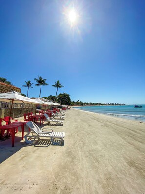 A beach with sun loungers and umbrellas, a clear sky, and a calm sea. - Bem Bahia Hotel (Santa Cruz Cabralia)