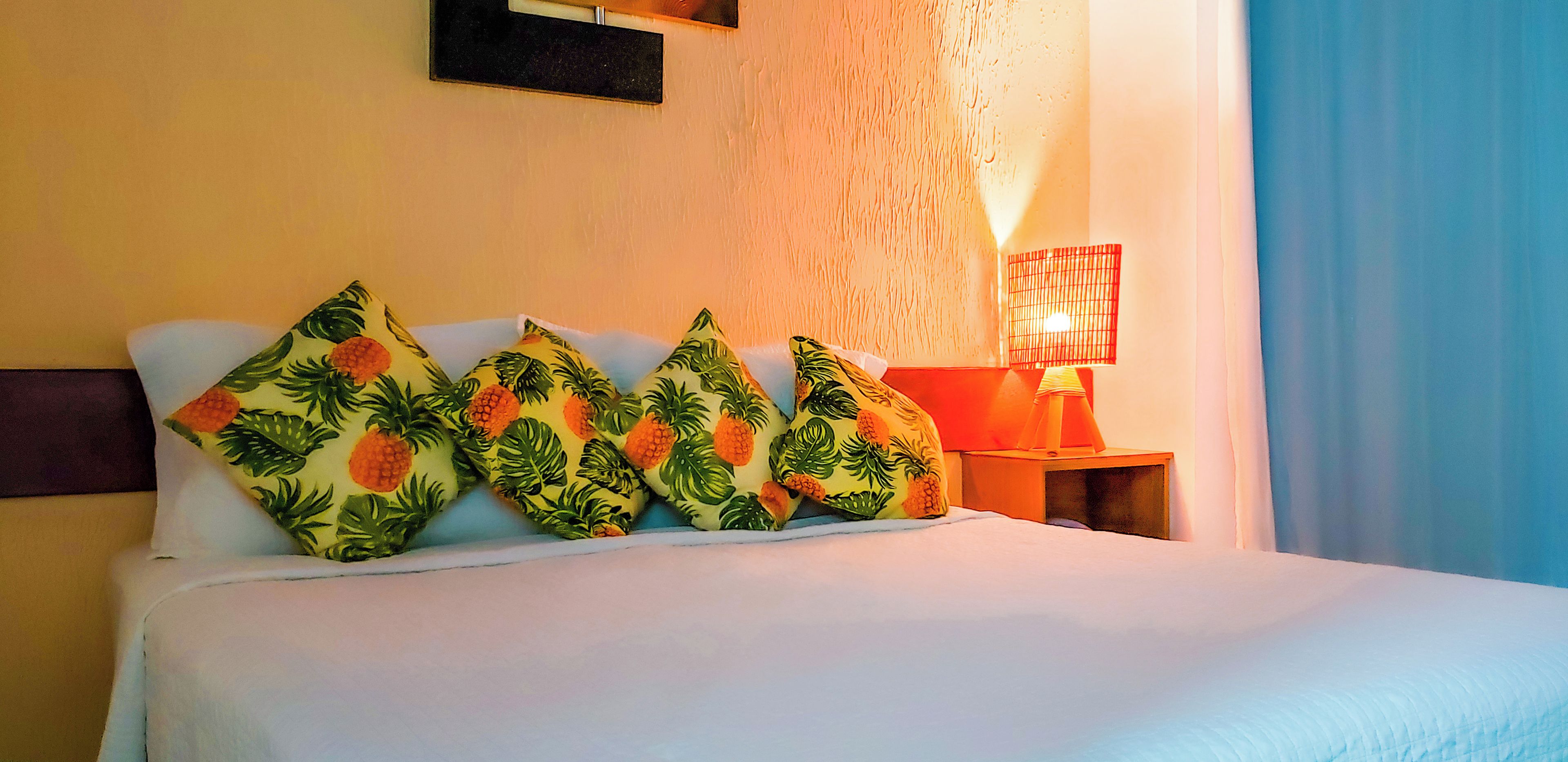 Un lit avec une literie blanche et quatre coussins décoratifs ornés d’un motif de feuilles tropicales.
