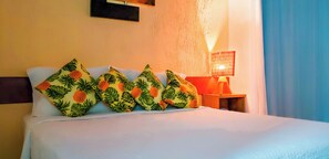Una cama con ropa blanca y cuatro almohadones decorativos con estampado de hojas tropicales.
